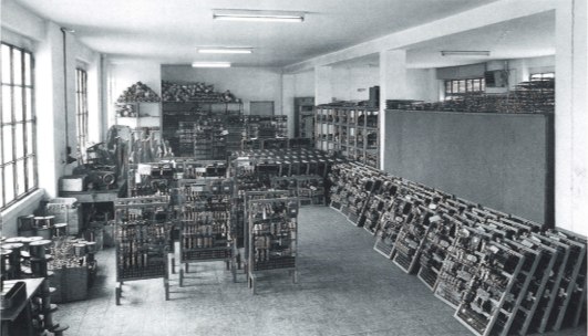 Foto d'epoca della produzione Bassetti Elevatori: reparto con quadri di manovra su carrelli e appoggiati alle pareti