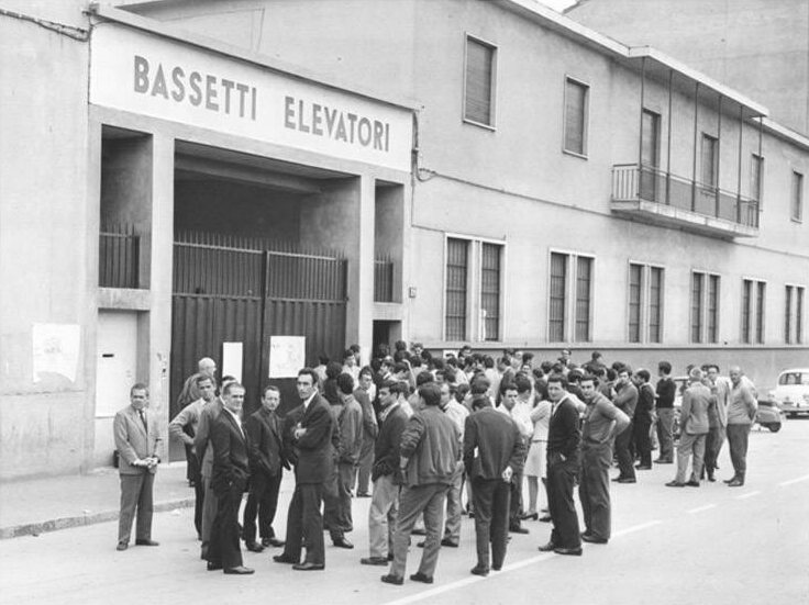 Foto d'epoca in bianco e nero: un gruppo di persone davanti alla storica sede della Bassetti Elevatori in via Sangro 29 a Milano