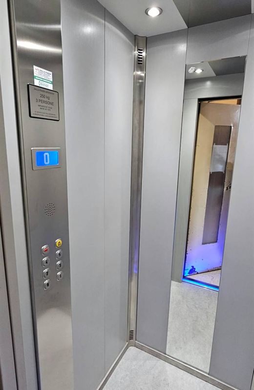 Cabina di ascensore con pareti grigie, pulsantiera in acciaio con display di piano e specchio