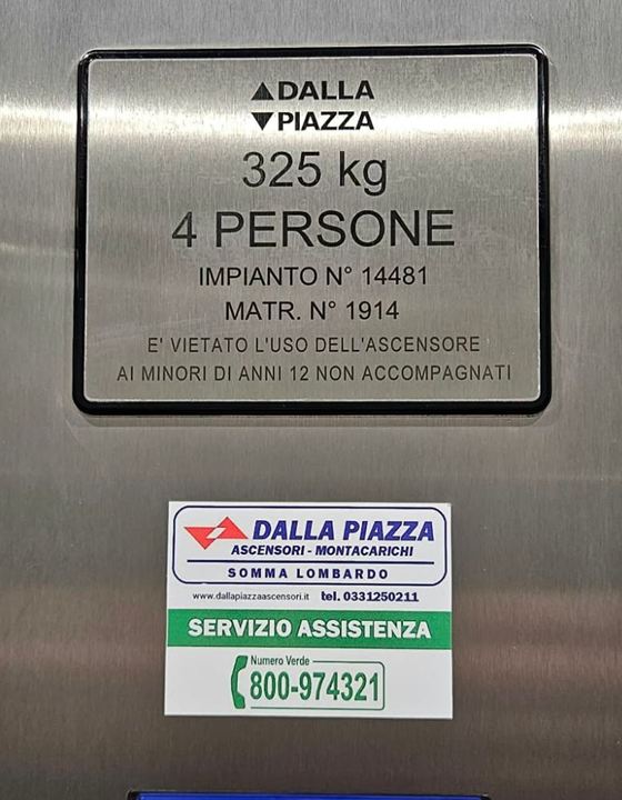 Targa di cabina Dalla Piazza (325 kg, 4 persone) e, sotto, l'adesivo del servizio assistenza con il numero verde 800-974321