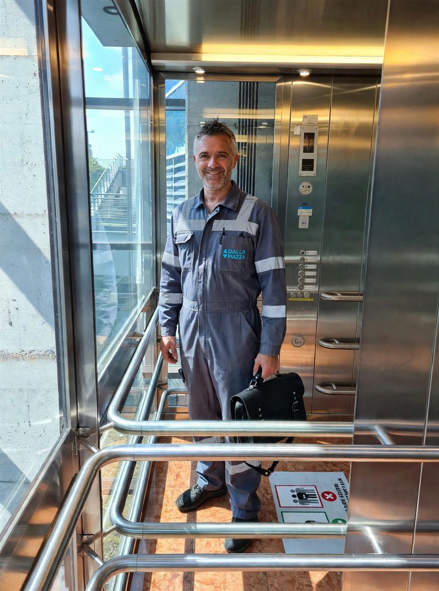 Tecnico Dalla Piazza in tuta da lavoro con il logo aziendale, dentro la cabina panoramica di un ascensore