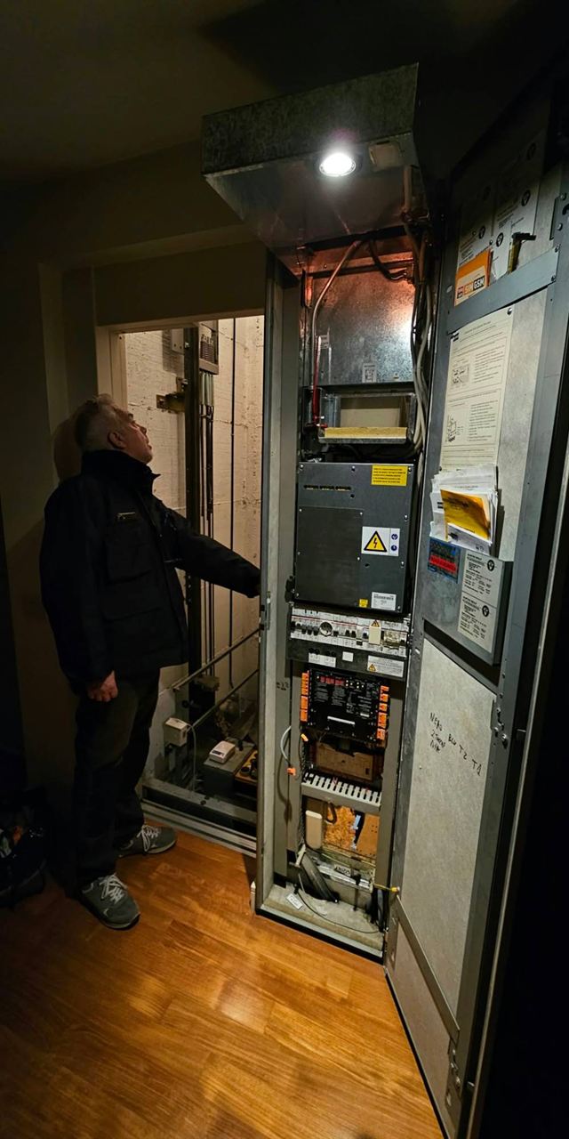 Tecnico al lavoro davanti al quadro di manovra aperto, accanto al vano dell'ascensore
